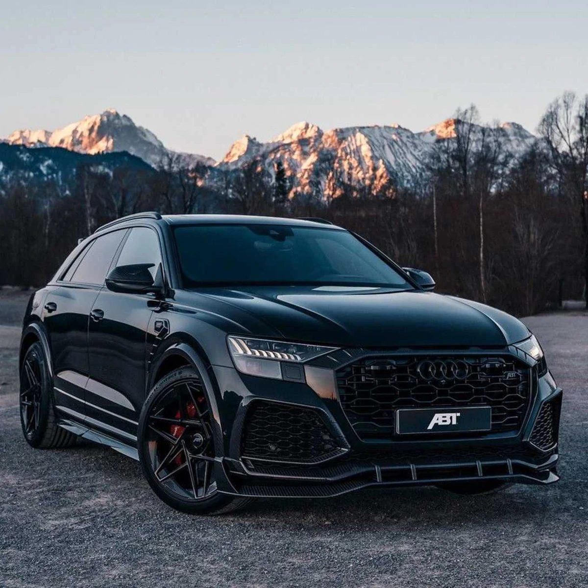Zwarte Audi SUV voor besneeuwde bergen bij zonsondergang